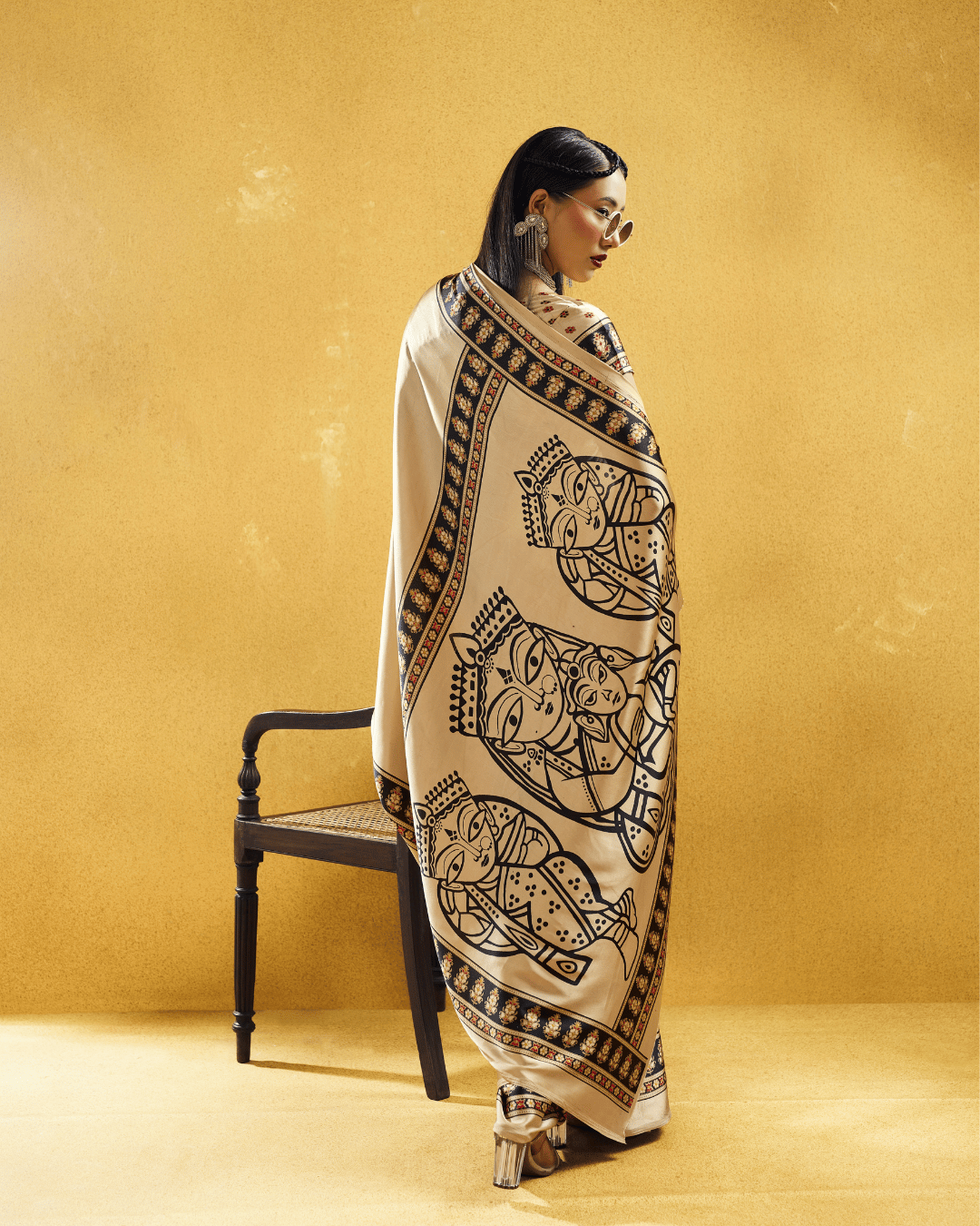 Back view of the model showing the drape of the ivory-beige pre-draped saree, framed by patterned borders and oversized figurative motifs.