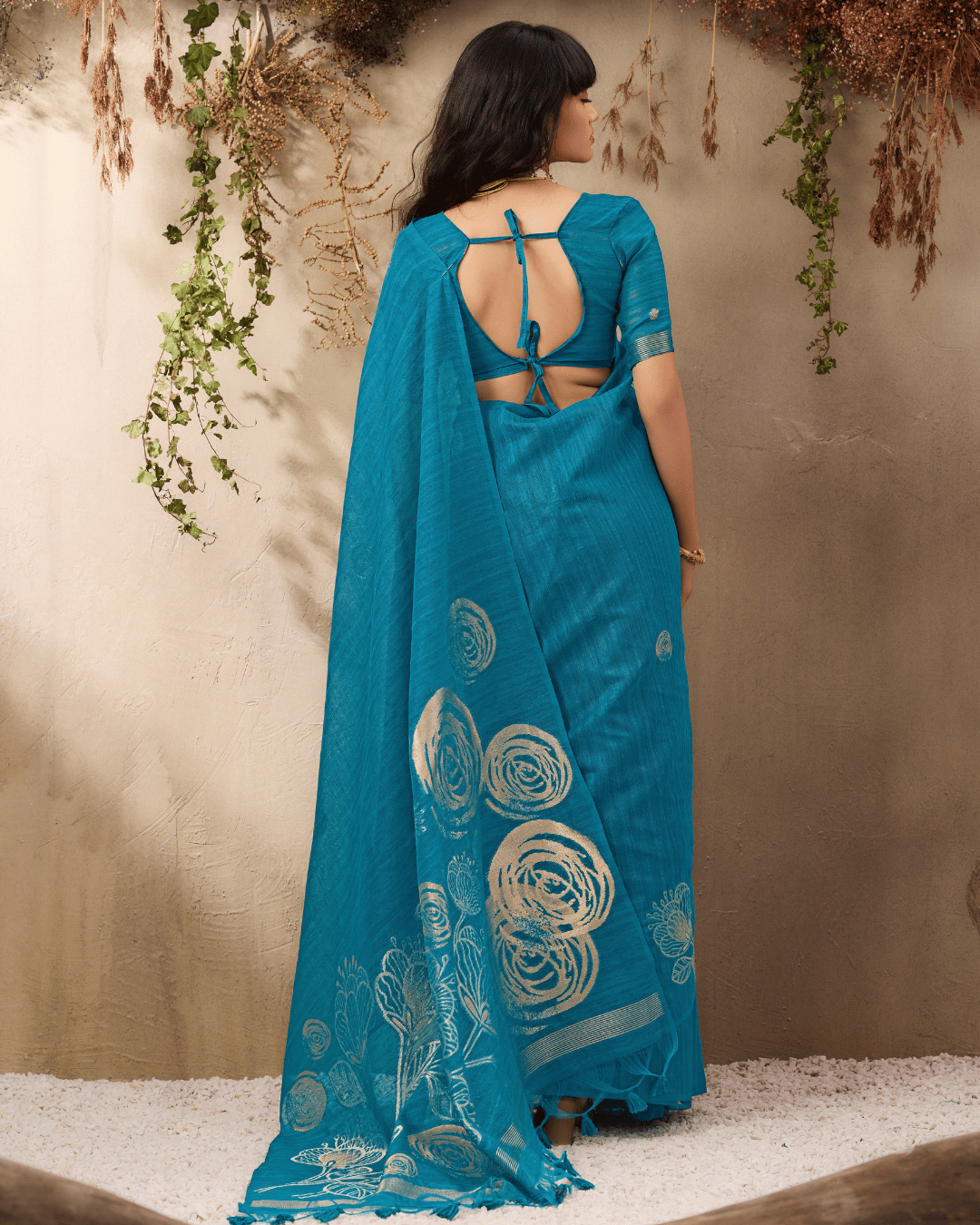 Back view of the model displaying the subtle body motifs and the broad spread of the gold-outlined floral pallu with teal tassels.