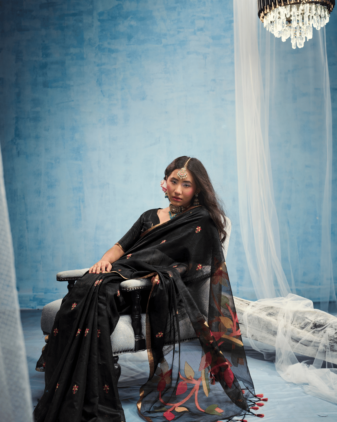 Model seated on a chair showcasing the pre-set pleats and the flow of the sheer pallu draped gracefully over the side.