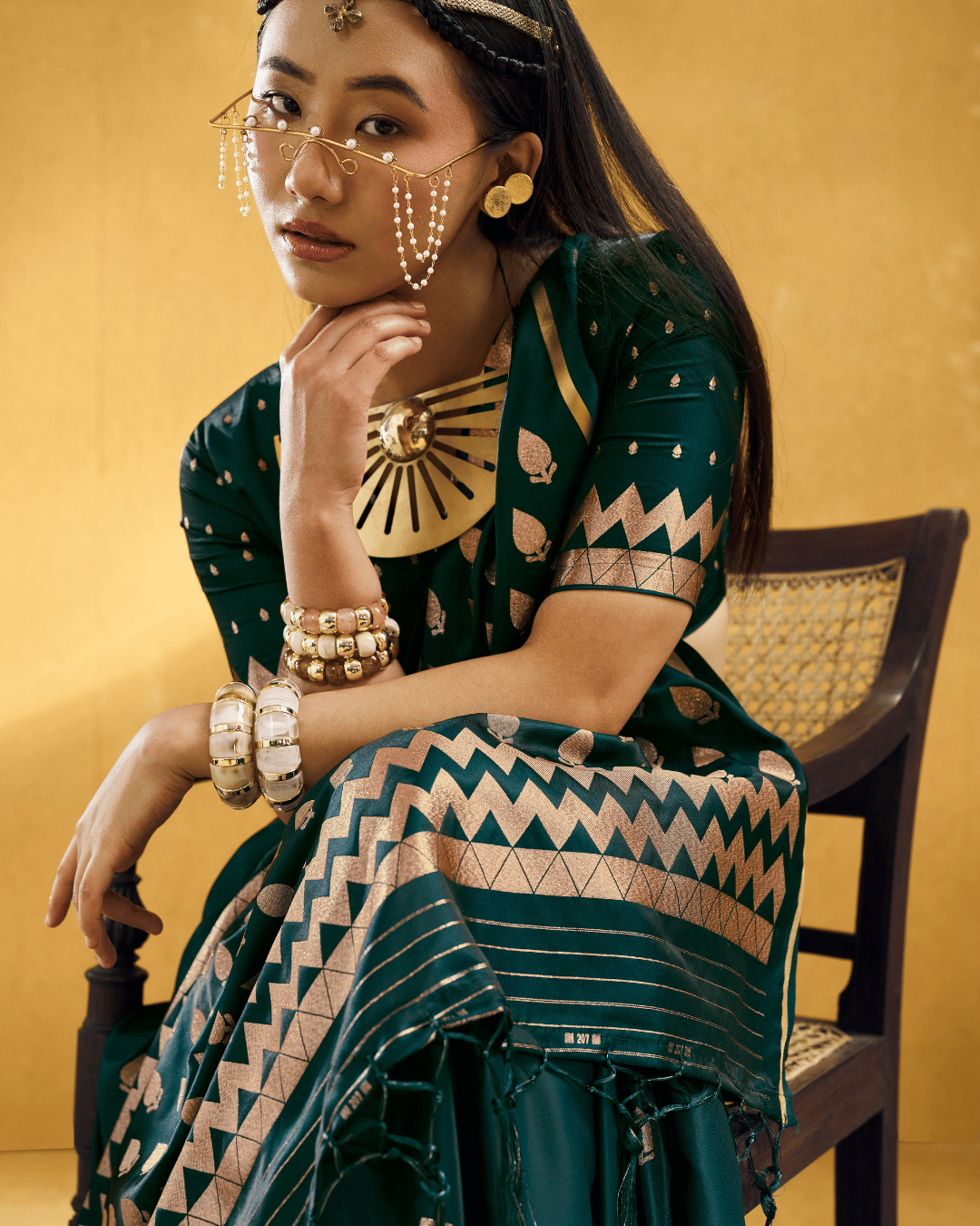 Close-up seated portrait of a model in the Forest Green Chevron powerloom silk ready-to-wear pocket saree, displaying gold leafy motifs and a bold chevron zigzag border of the ready to wear pocket saree.