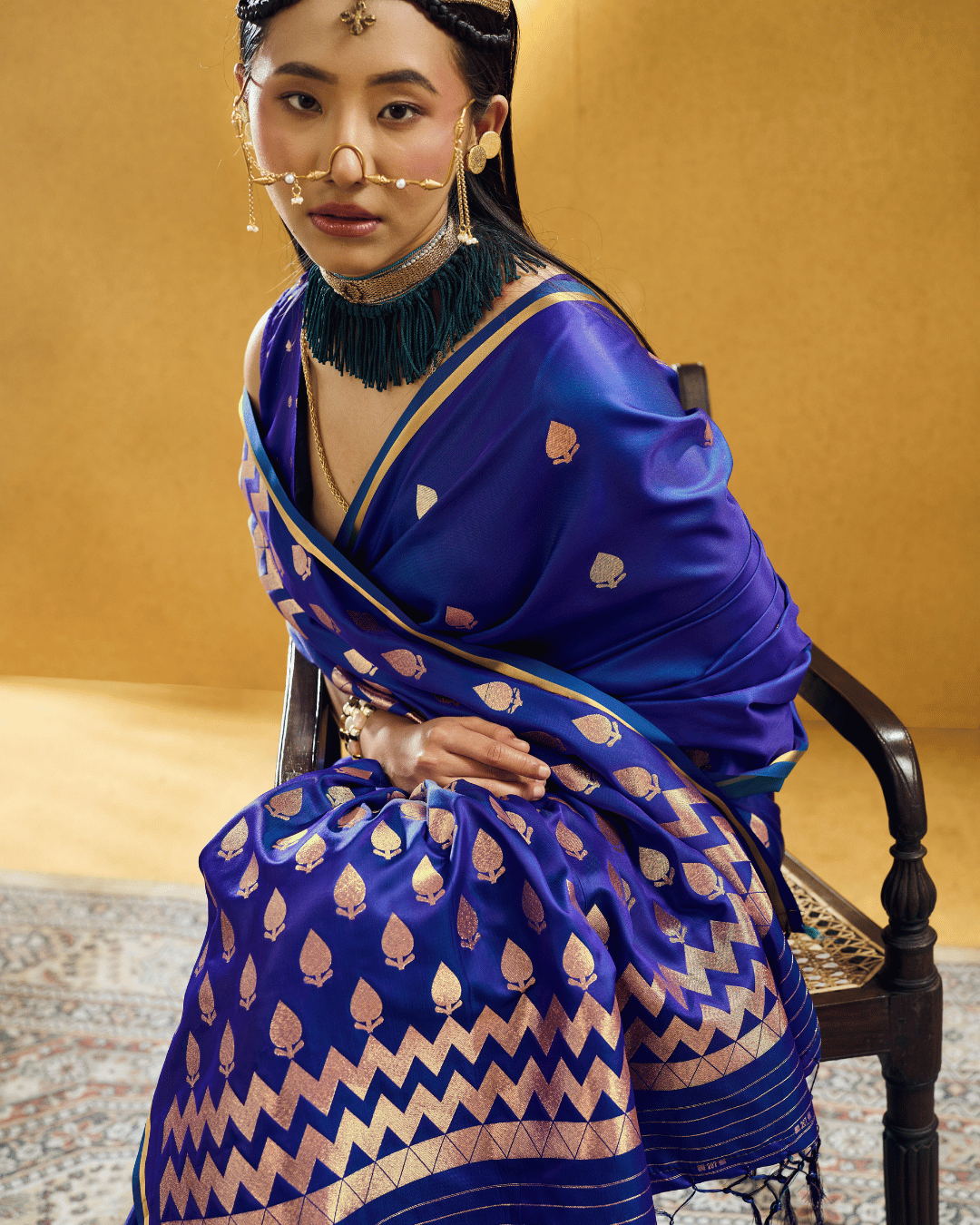 Close-up seated shot of the model wearing the Royal Blue Chevron ready-to-wear pocket saree, highlighting the lustrous satin finish, champagne-gold woven leaf bootas, broad chevron border, fine horizontal pallu stripes, and dark tassels.