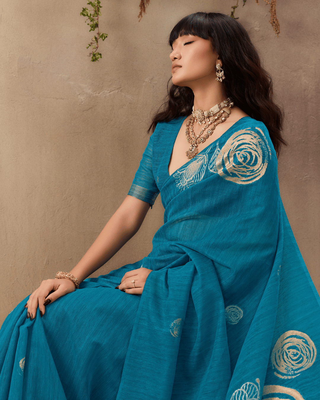 Seated profile shot highlighting the rich teal texture and delicate circular motifs scattered across the body of the pre-draped saree.