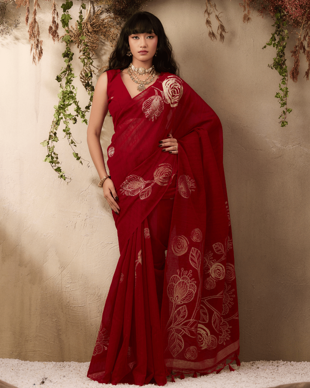 Full-length portrait of the model wearing the deep red pre-draped pocket saree with scattered gold circular body motifs and an open pallu adorned with large botanical line-art artwork.