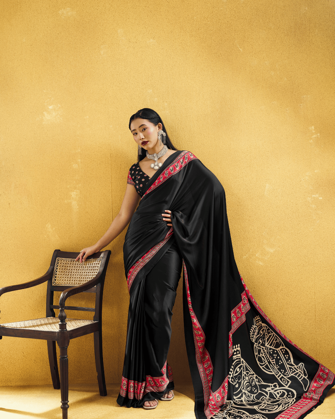 Black ready-to-wear saree with a printed red border and a statement pallu featuring large folk-art motifs.