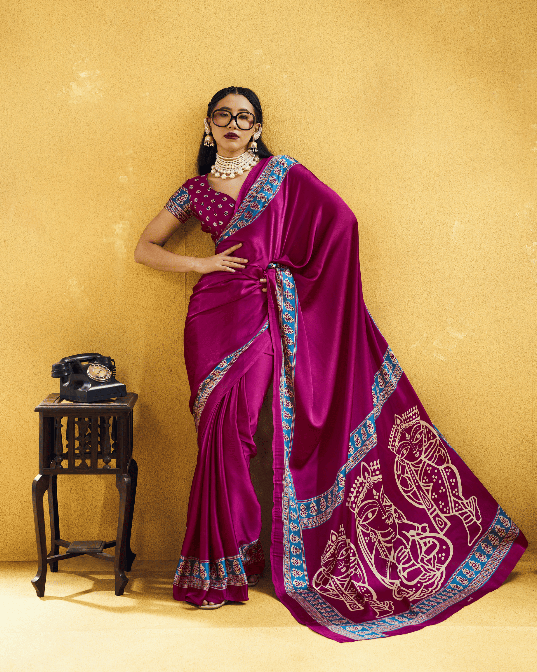 Full-length view of a model in a vibrant magenta ready to wear pocket saree with bright blue patterned borders and large ivory-toned figurative pallu artwork.