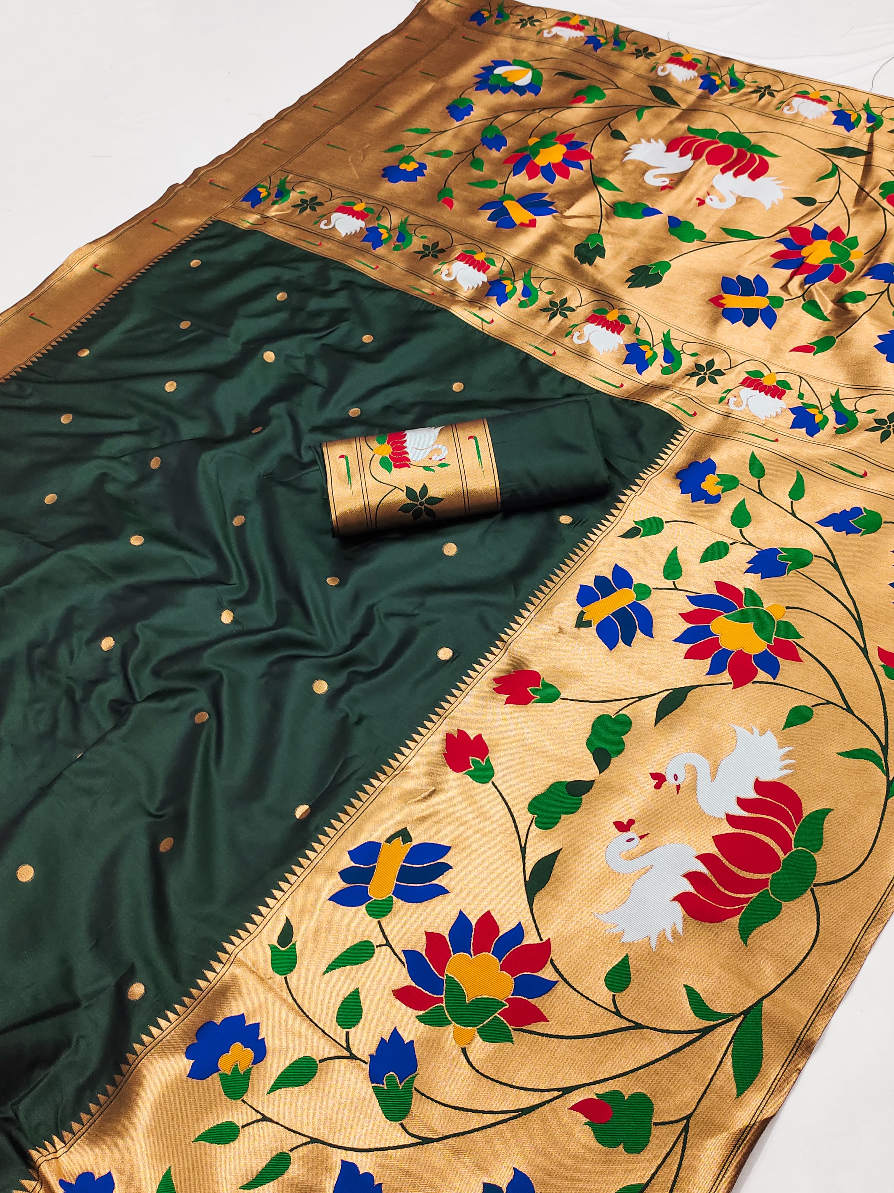 Flat lay of a deep green Paithani silk saree showcasing scattered gold boti motifs, a gold-toned border, and an elaborate floral pallu with white swan motifs.