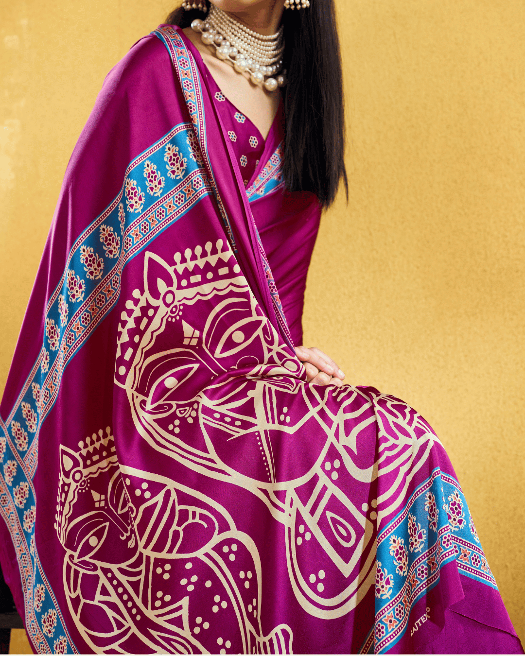 Detailed shot of the pallu highlighting large ivory folk-art motifs on a rich magenta base with printed bright blue borders.
