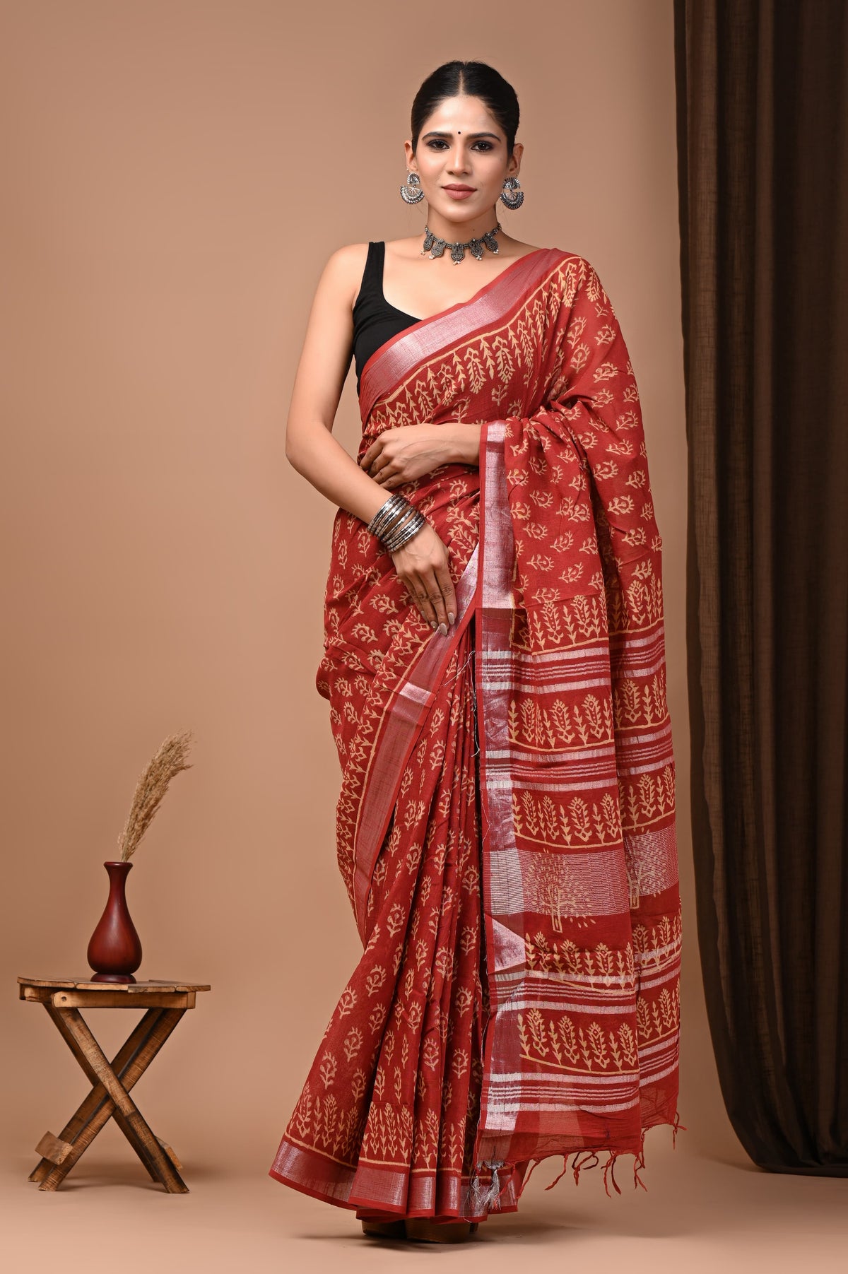 Full-length shot of a model in the Root & Rhythm rich red linen ready-to-wear pocket saree, displaying pre-stitched pleats with cream botanical sprig motifs, silver borders, and a graphic striped pallu with red tassels.