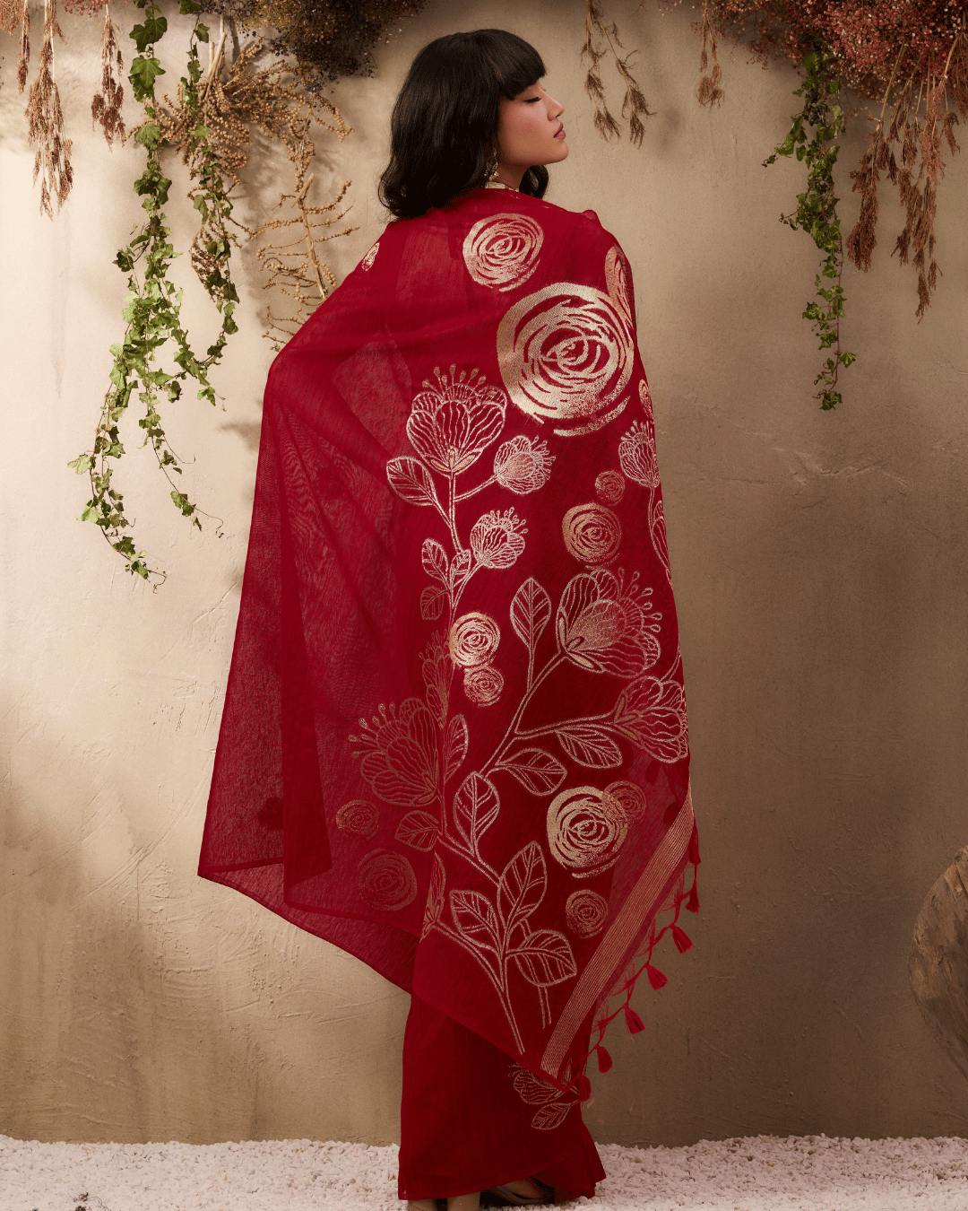 Back view of the model displaying the deep red pallu, showcasing the detailed gold-toned line artwork, narrow striped hem border, and red tassel fringe along the bottom edge.