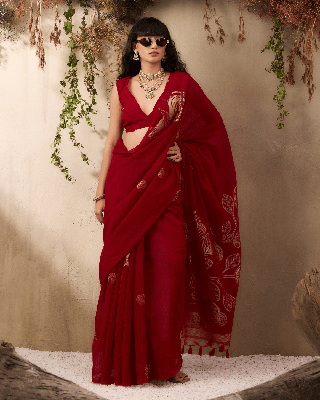 Model wearing the pre-draped ruby-red saree highlighting the neat front pleats, gold body motifs, and fluid pallu fall.