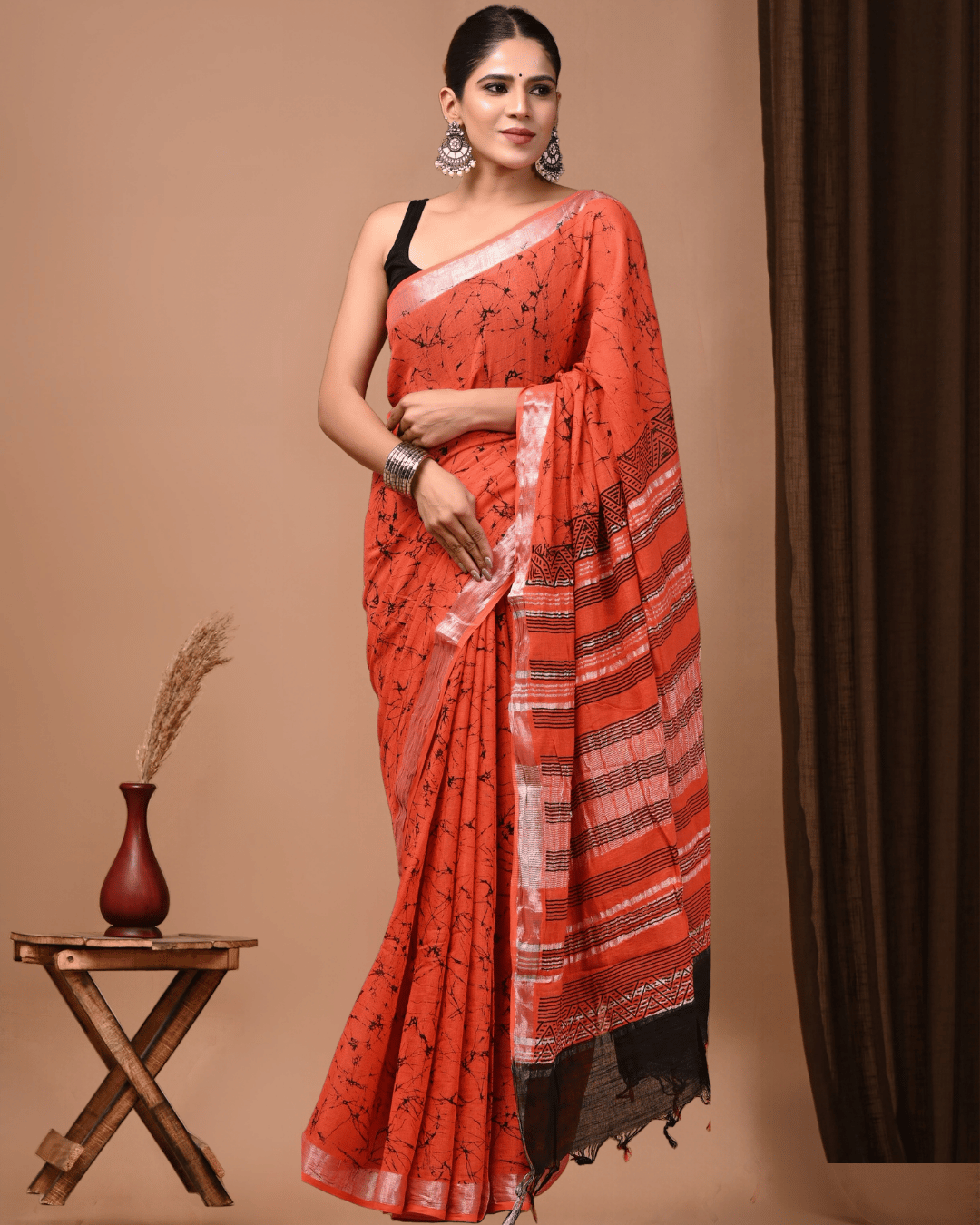 Sandal Noir linen ready to wear pocket saree in coral orange with black branching patterns, striped geometric pallu and black tassel detailing.
