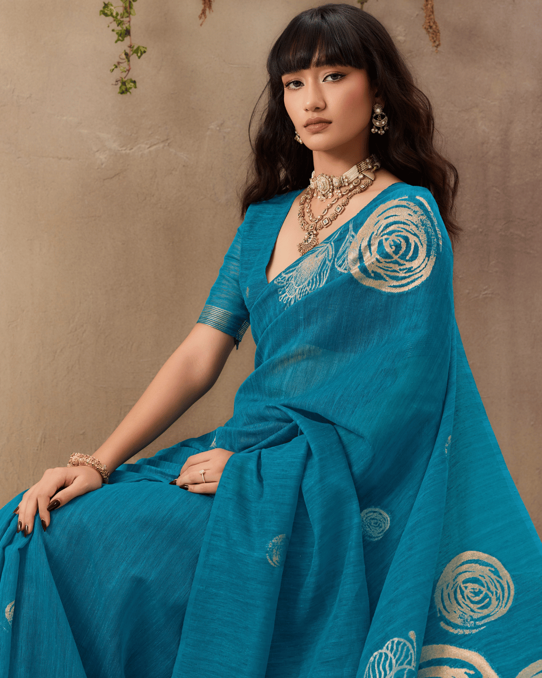 Model seated in a half-length pose wearing the vibrant teal munga-silk saree showing the gold line-art rose motifs.