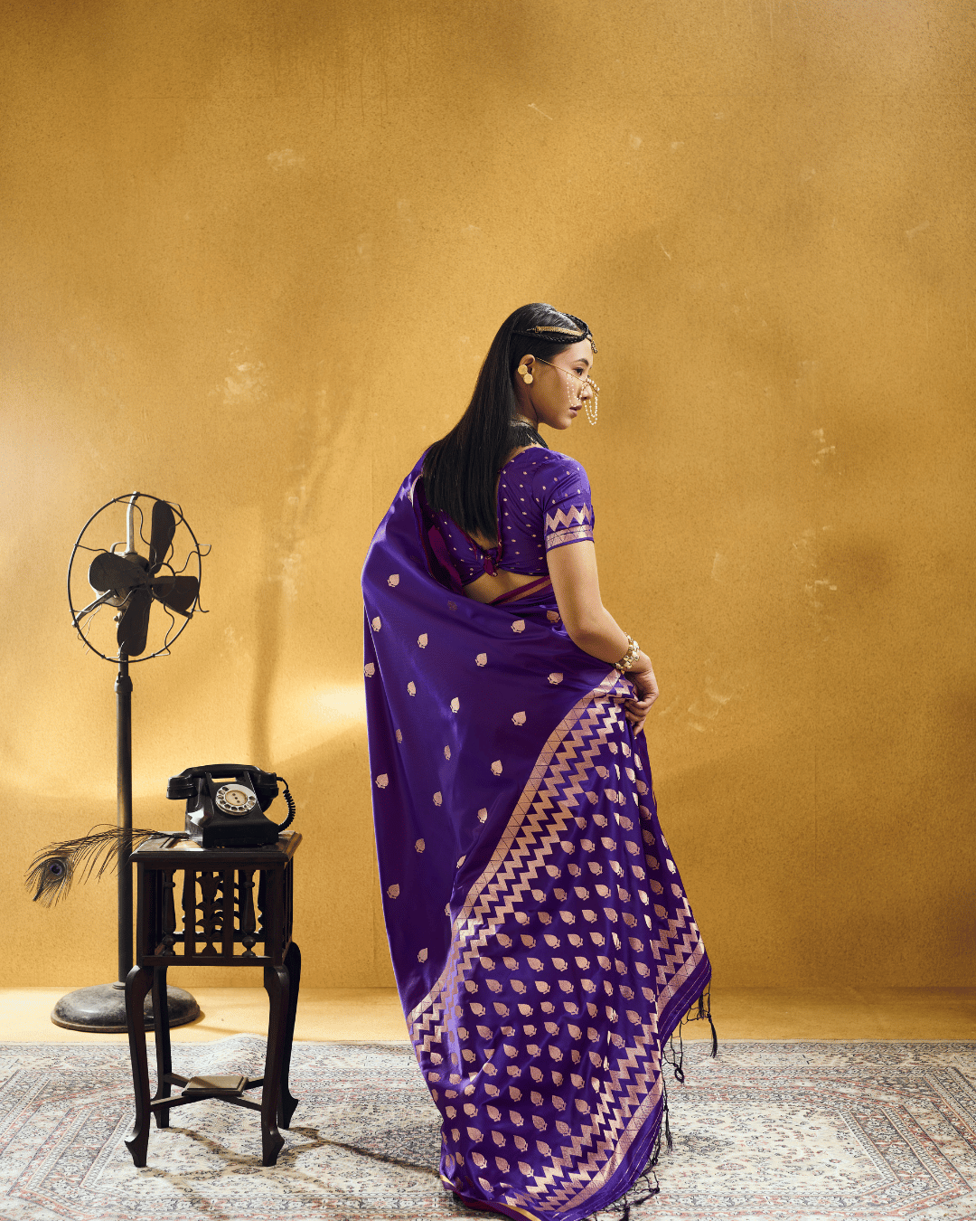 Back-angle full-length shot showcasing the grand graphic pallu of the violet-purple satin ready-to-wear pocket saree, featuring dense rows of gold leaf motifs framed by multi-tiered chevron borders and dark edge tassels.