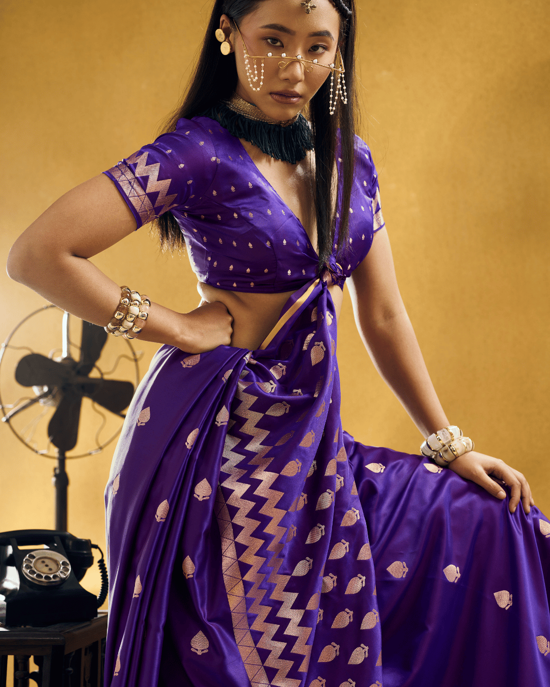 Close-up waist-up shot of the model wearing the violet-purple ready-to-wear pocket saree, highlighting the lustrous satin fabric, warm gold woven leafy bootis, chevron zigzag pallu bands, and gold border.