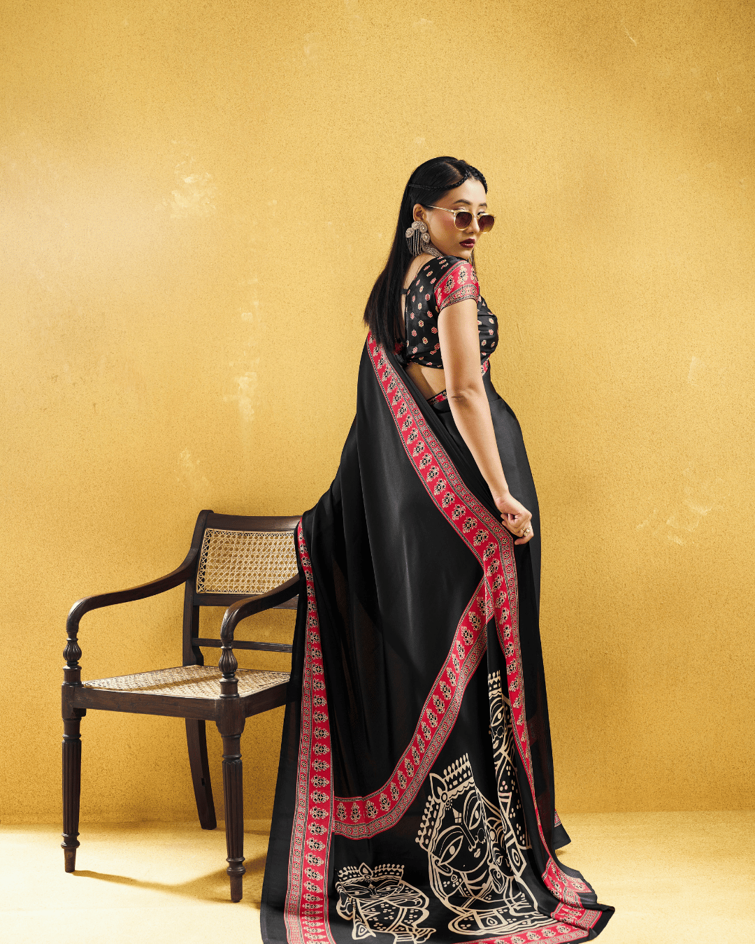 Back view of a model in a sleek black ready to wear pocket saree highlighting the vibrant red printed border and dramatic artwork on the flowing pallu.