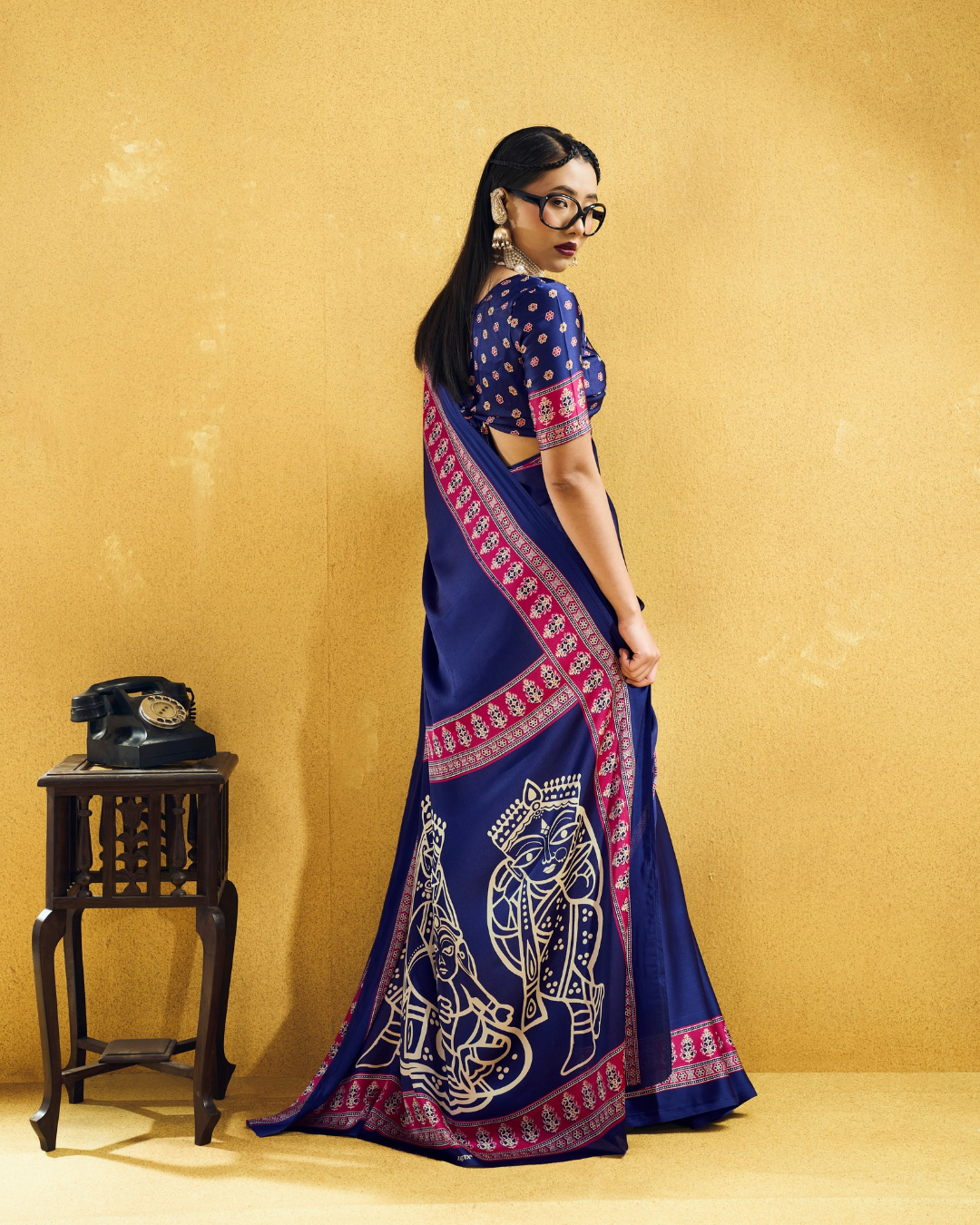 Back view of a model in a deep navy blue saree showing the magenta printed trim and figurative pallu artwork.