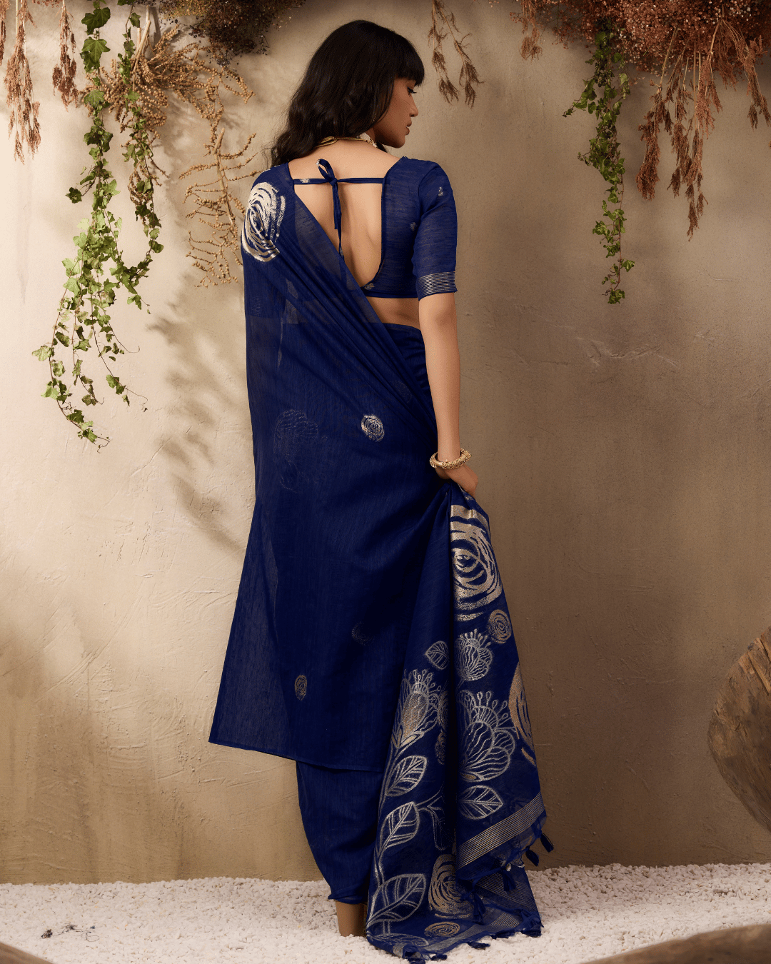 Back view of the vine and verse pre-draped pocket saree, emphasizing the elegant movement of the gold botanical pallu and dark navy tassels.