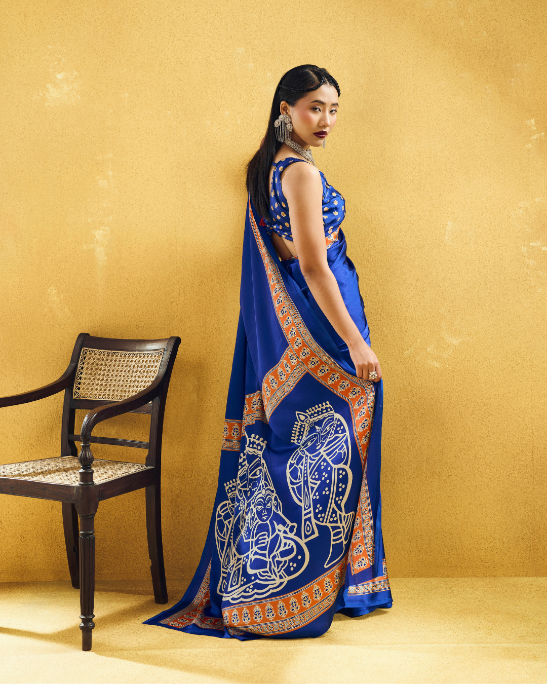 Back view of the model demonstrating the smooth drape of the blue pre-draped saree, displaying the framed orange border trim and figurative pallu motifs.