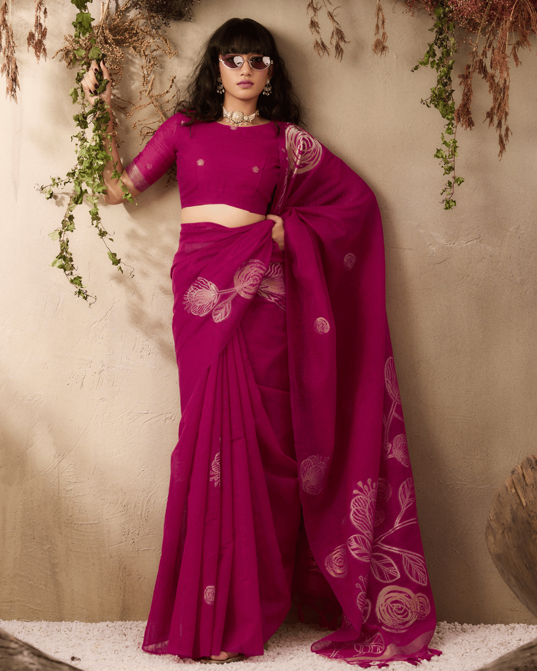 Full-length portrait of the model showing the complete drape of the berry-magenta pocket saree, featuring pre-set pleats and large gold botanical sketch motifs flowing down the pallu.