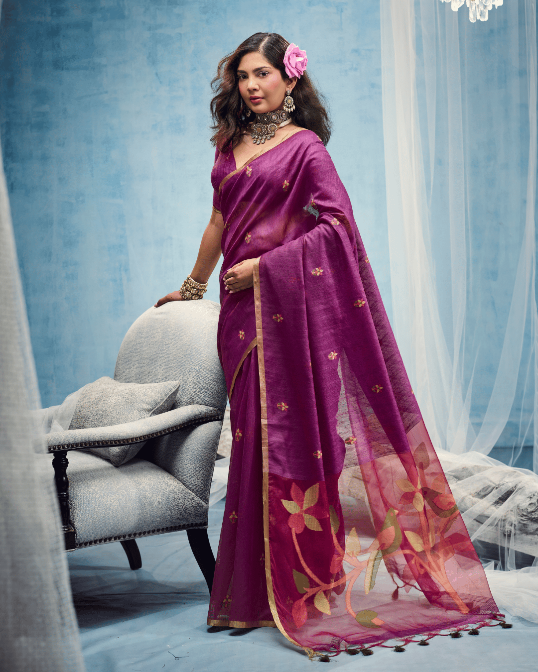 Full drape of the deep berry-purple saree with pre-set pleats, delicate scattered motifs, and an open sheer pallu with botanical vine designs and green tassels along the edge.