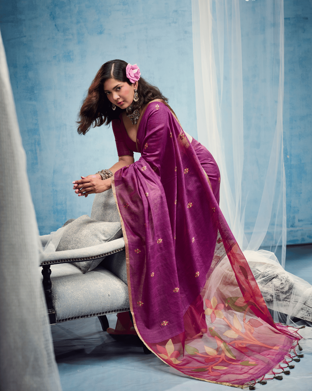 Model leaning gently on the armrest of a chair, displaying the graceful drape of the ready to wear pocket saree, small floral dots across the purple body, and the extended patterned pallu.