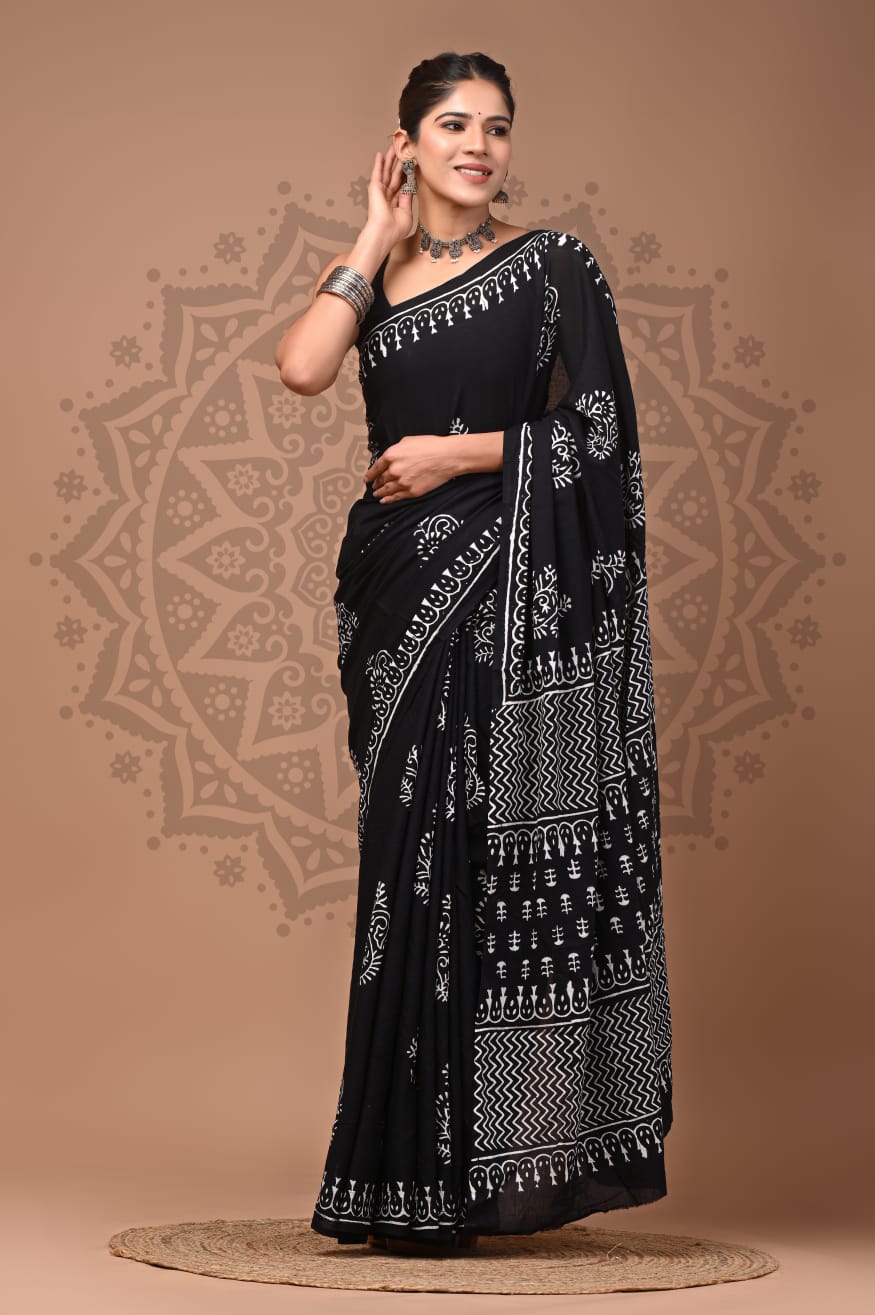 Full-length portrait of a model wearing the black and ivory Mul Cotton ready-to-wear pocket saree, featuring scattered white floral-leaf motifs, pre-stitched pleats, a teardrop-accented white border, and a zig zag patterned pallu.