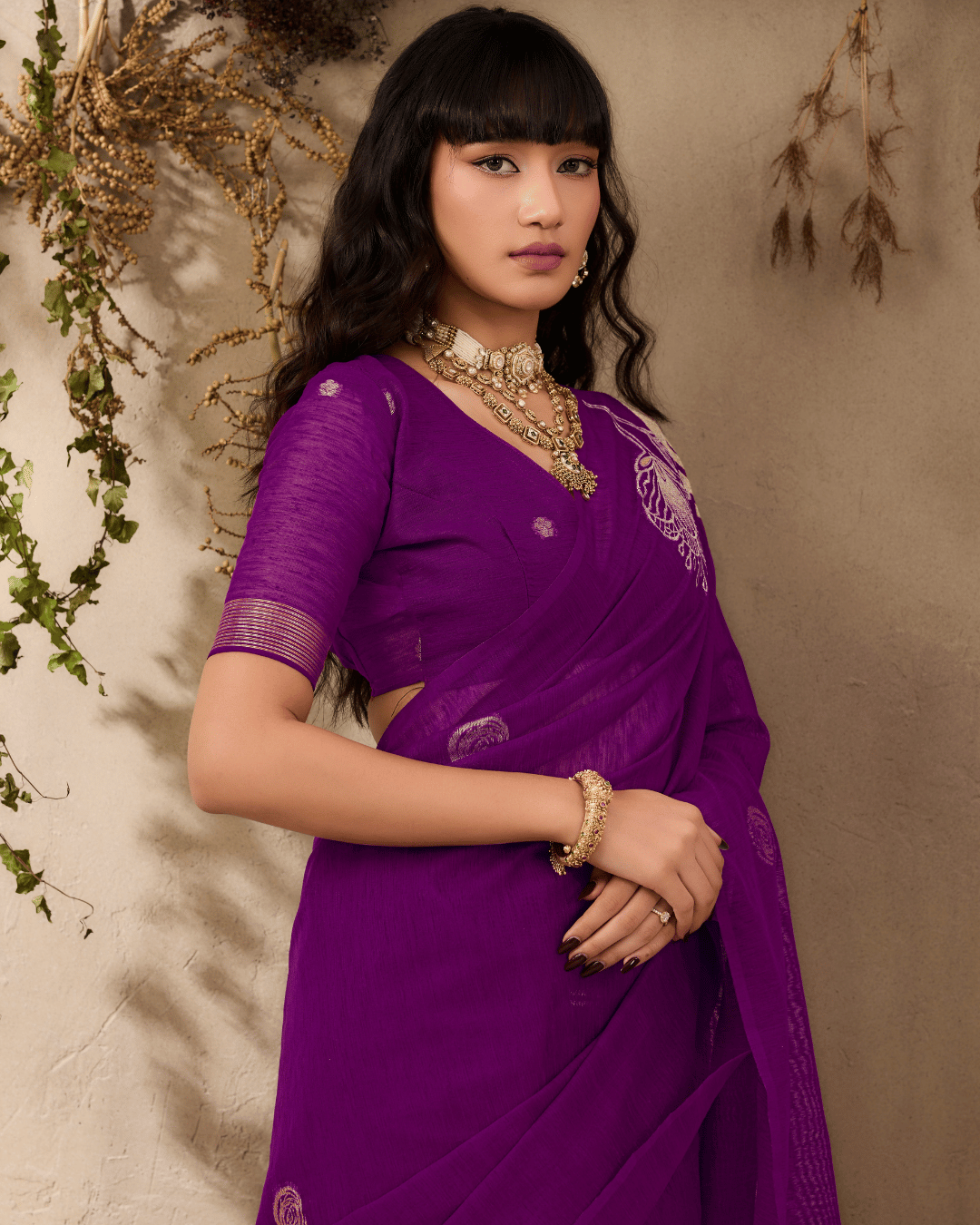 Model posing in a three-quarter view wearing a rich purple munga silk-inspired saree, highlighting the soft gold sketch-style floral motif.
