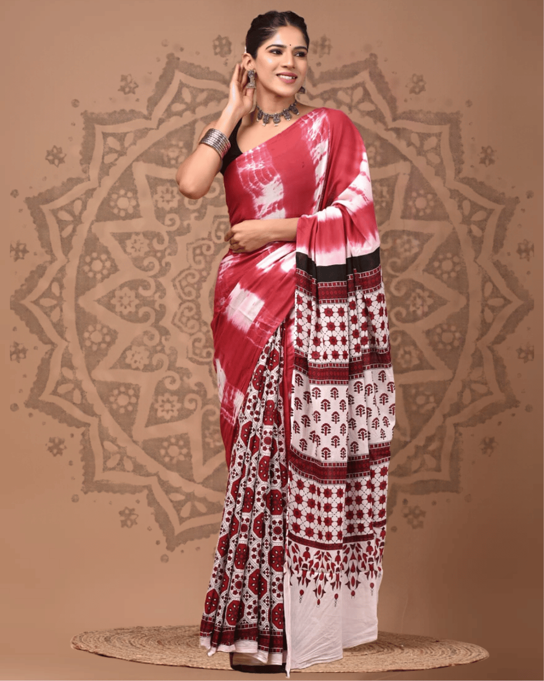 Model wearing a red, ivory and black Mul Cotton saree with white tie-dye-style patches, geometric lower panels, floral pallu sections and a patterned border
