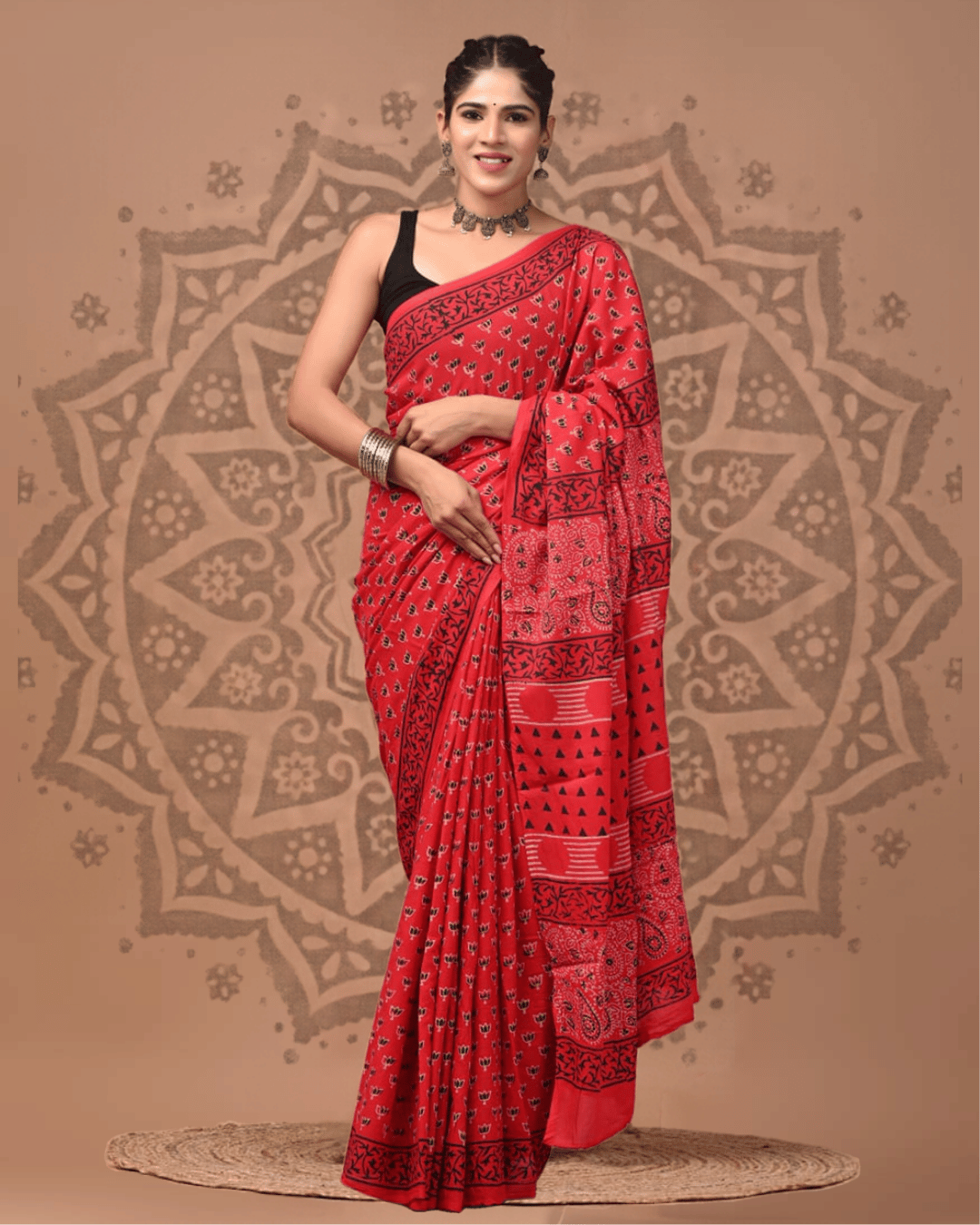 Crimson red Mul Cotton ready-to-wear pocket saree with small black-and-white motifs, a dark leafy border, and a pallu featuring floral and paisley-like prints, horizontal stripes and rows of black triangles.