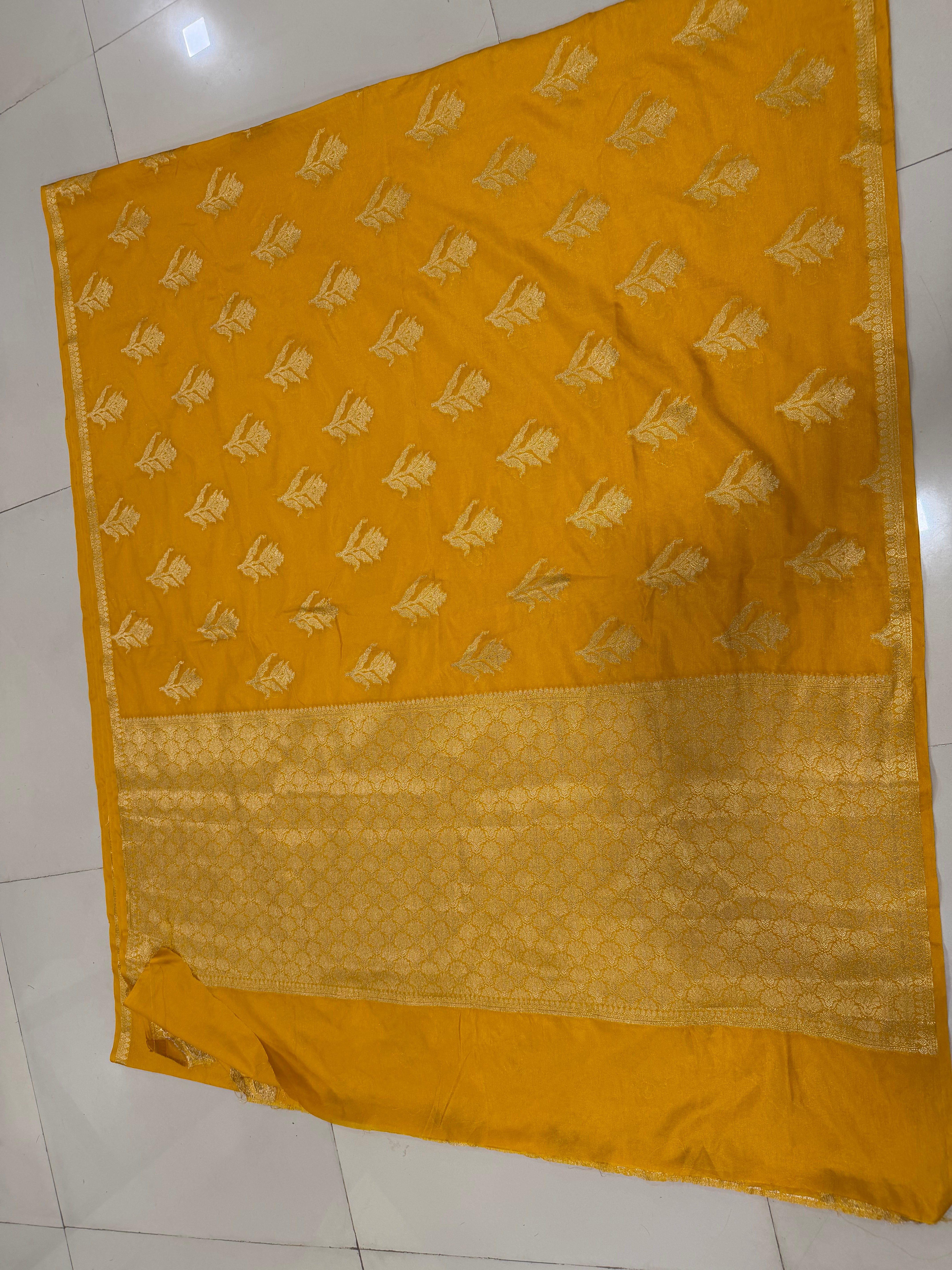 Flat lay view of the radiant mustard yellow Banarasi Katan Silk saree, displaying the scattered soft gold zari floral buttas across the body and the broad woven zari floral pallu panel framed by fine ornamental edges.