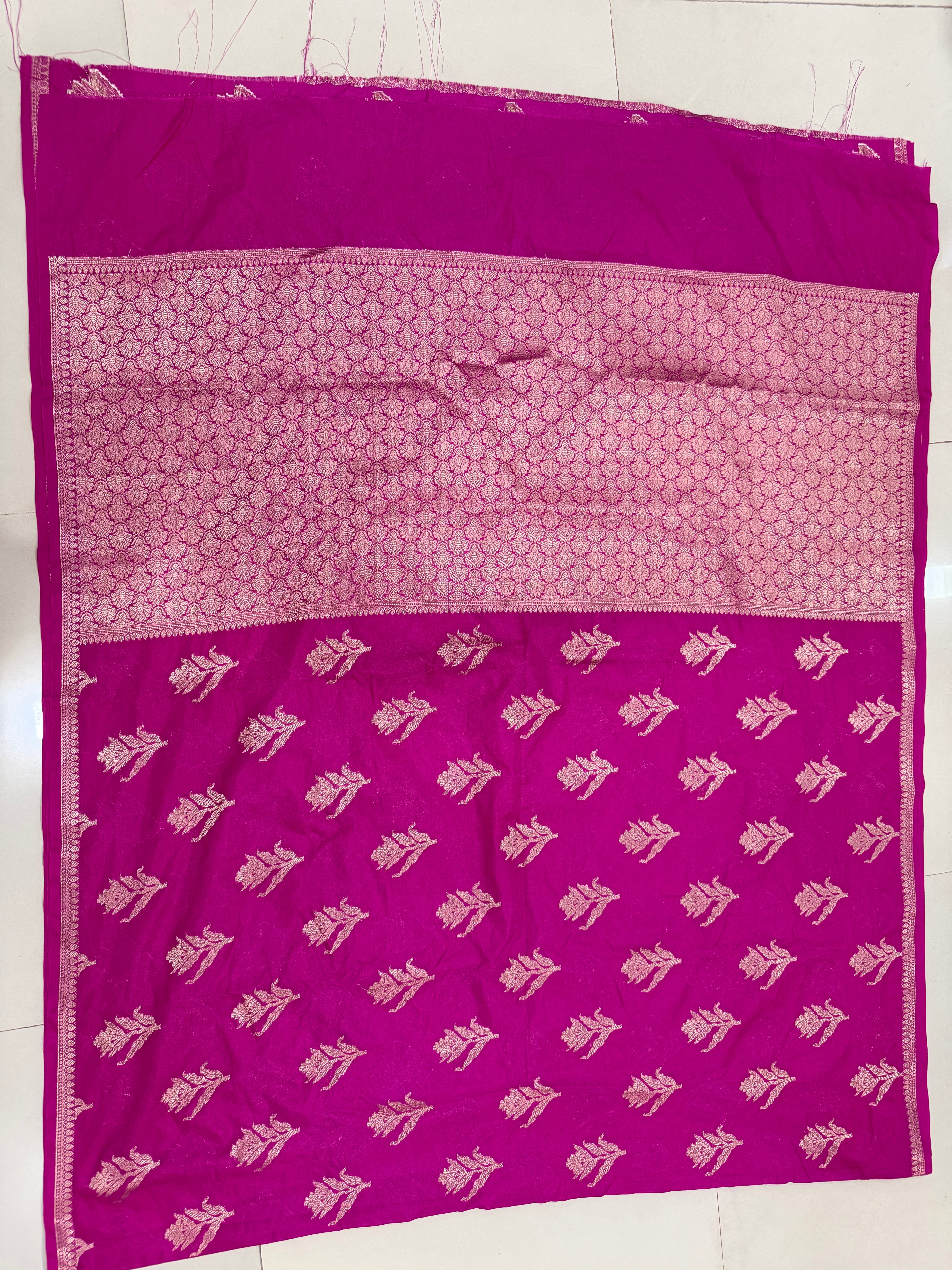 Flat lay view of the vibrant fuchsia pink Banarasi Katan Silk saree, displaying the scattered gold zari floral motifs across the body and the broad woven zari pallu panel framed by fine ornamental borders.