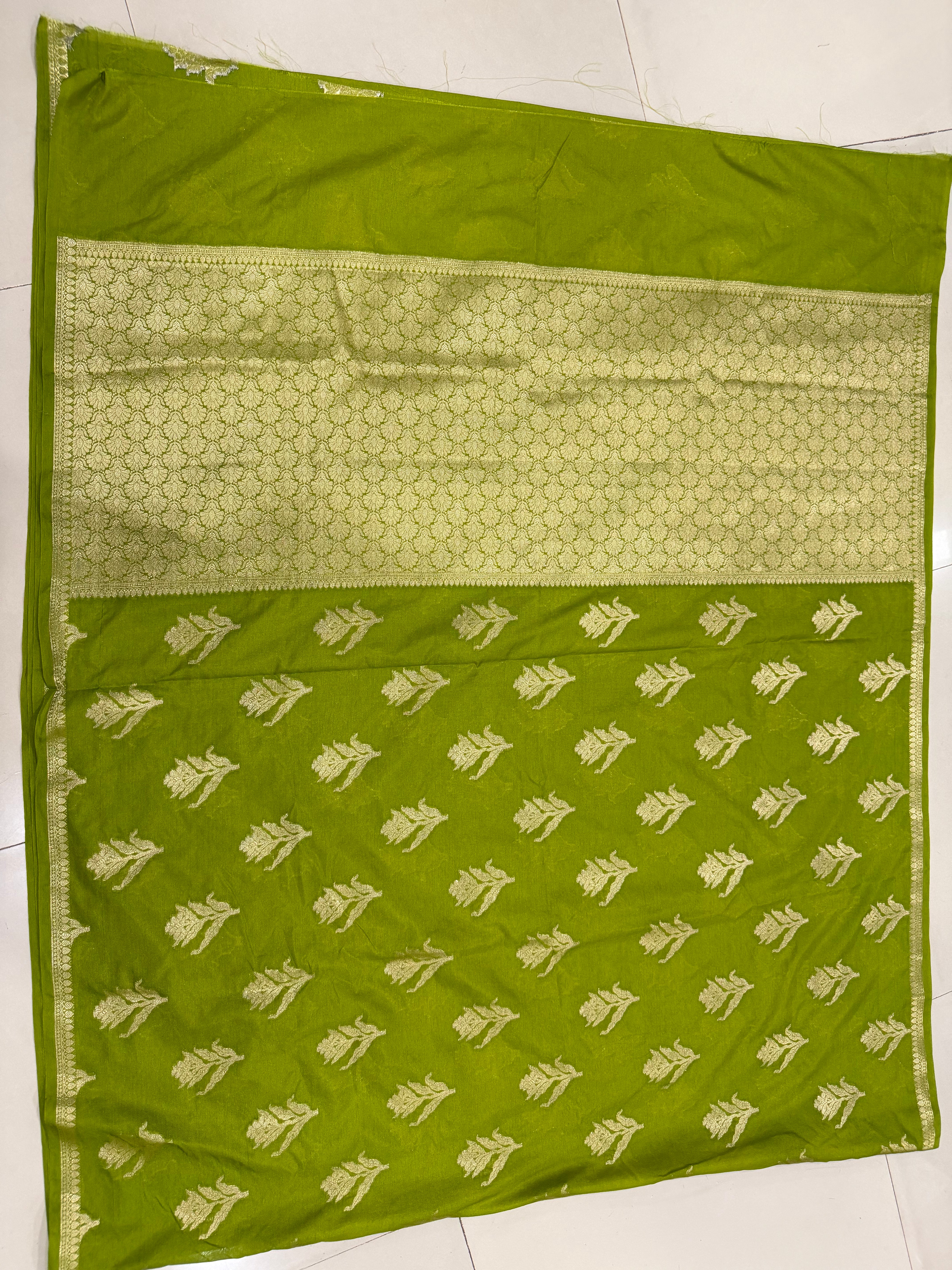 Flat lay view of the elegant olive green Banarasi Katan Silk saree, showing the evenly spaced gold zari floral buttas across the body and the intricate woven zari lattice pallu panel framed by fine linear borders.
