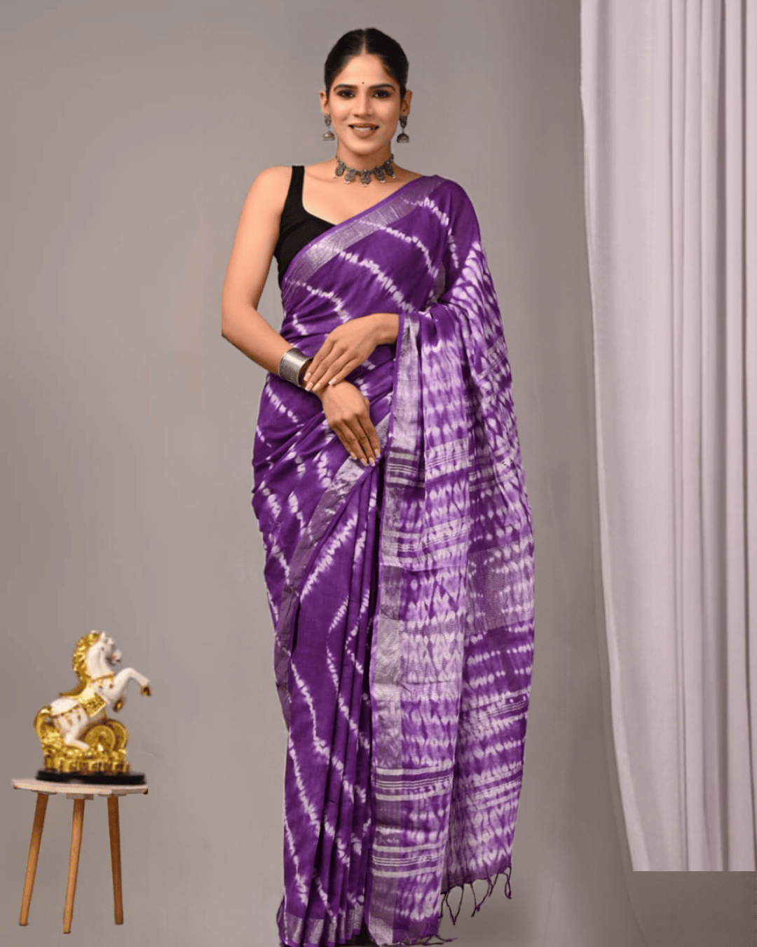 A model wearing Linen Muse purple linen ready-to-wear pocket saree featuring lilac-white diagonal tie-dye patterns, a striped pallu, contrasting border and matching tassels.