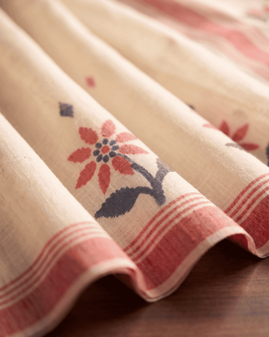 A close-up of the linen fabric of the ready-to-wear pocket saree, featuring a red and navy floral motif and a striped border