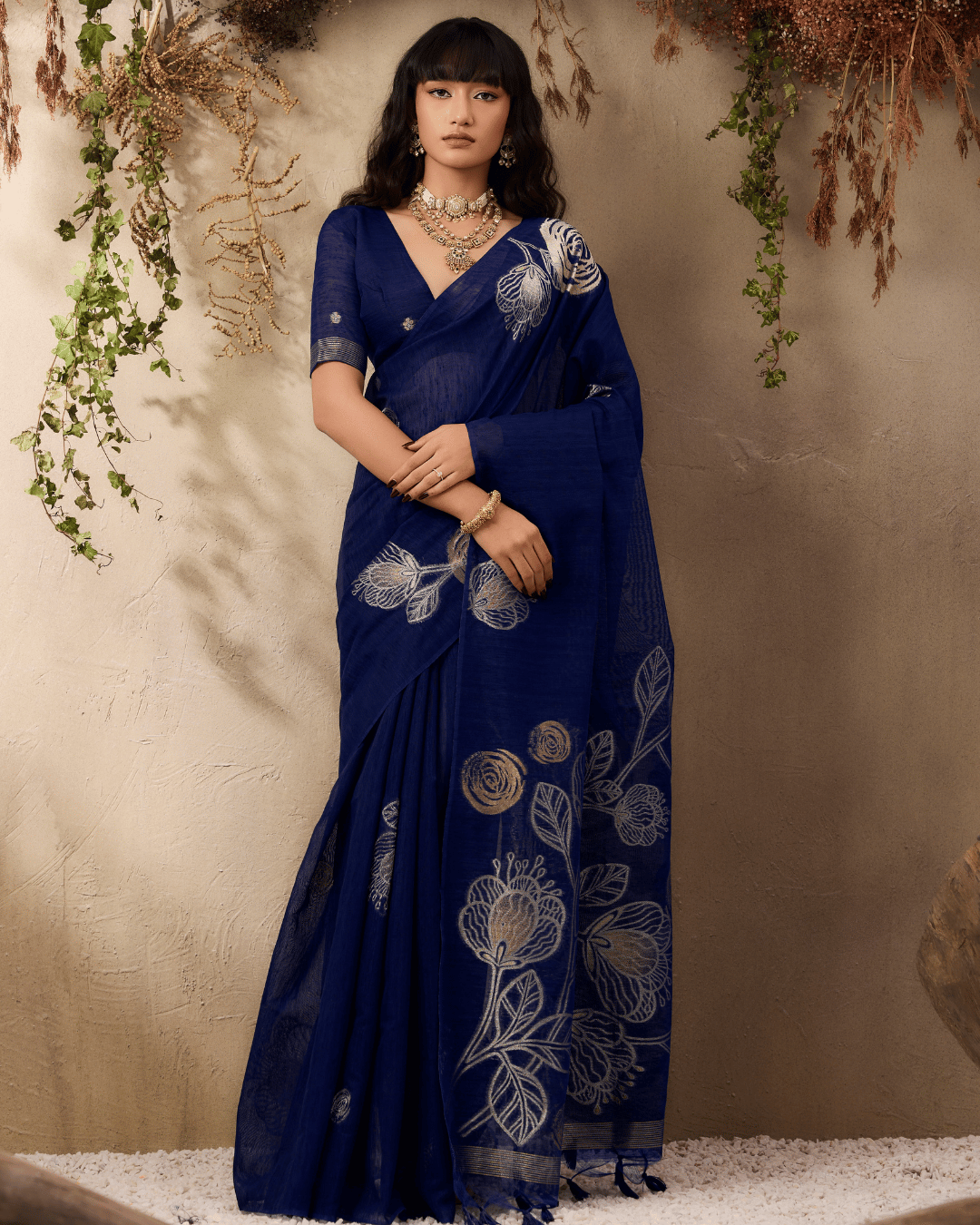Full-length portrait of the model displaying the complete pre-draped navy blue saree, featuring crisp front pleats, a clean body with subtle gold dots, and an open pallu adorned with large outlined flower-and-leaf artwork