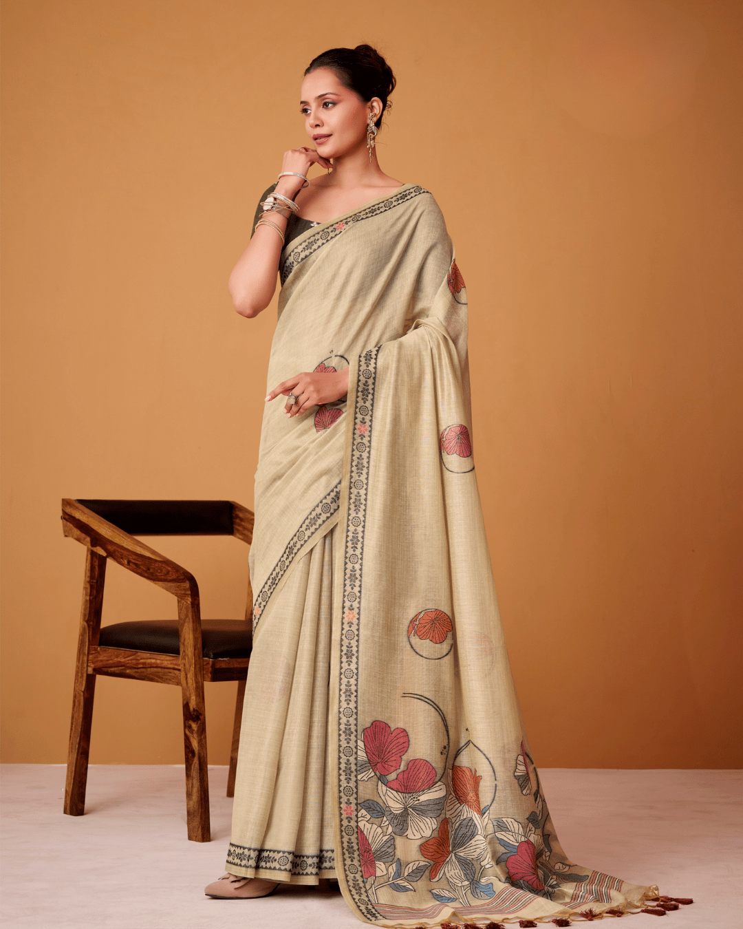 Full-length side-angle view of a model in the soft beige Petal Vines ready-to-wear pocket saree, showcasing pre-stitched pleats, coral floral motifs, charcoal border detailing, and a graphic floral pallu with deep rust tassels.