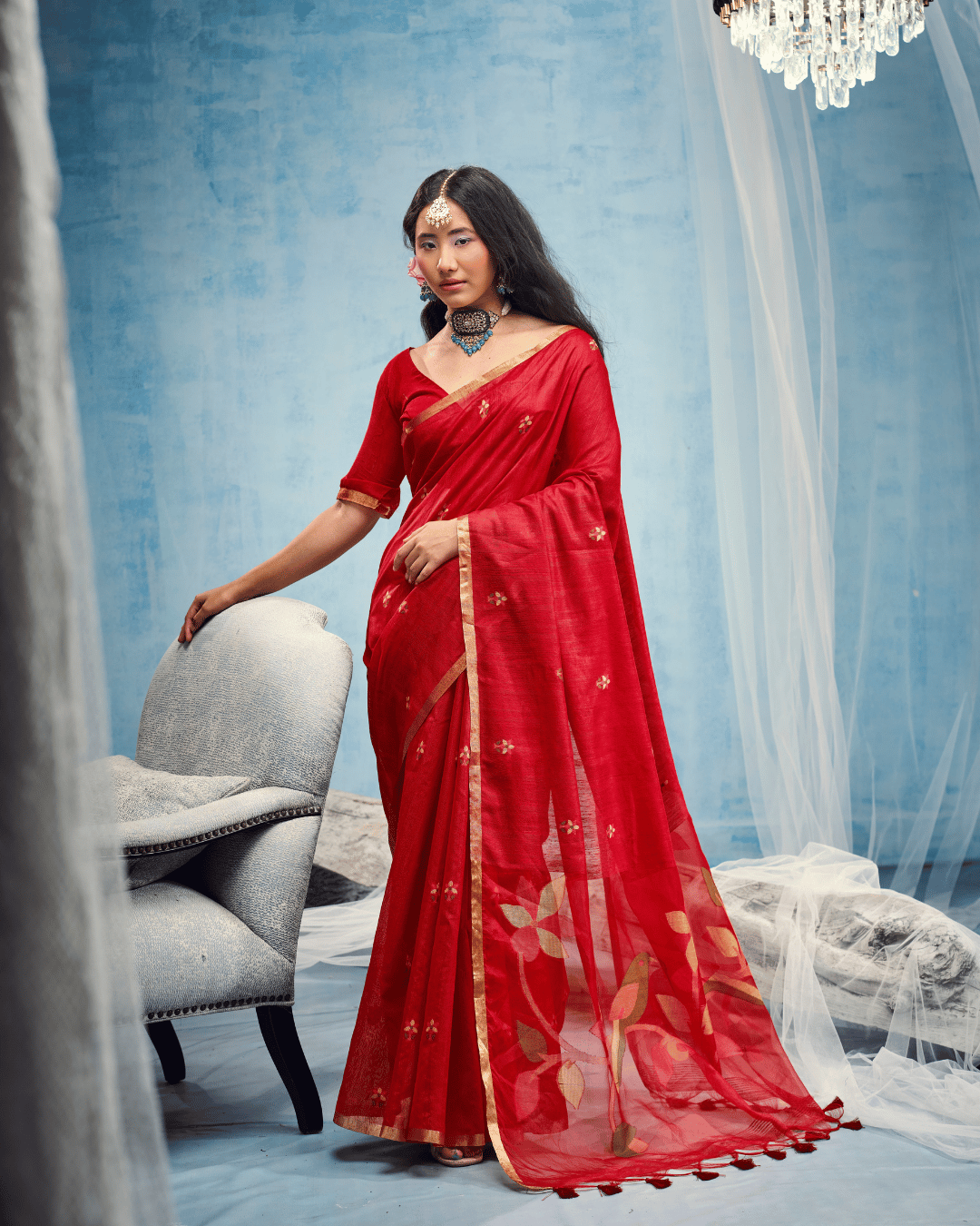 Full-length portrait of the model in the vivid red cotton saree, displaying the complete drape with pre-set front pleats, slim gold border, and open pallu with leaf motifs.   