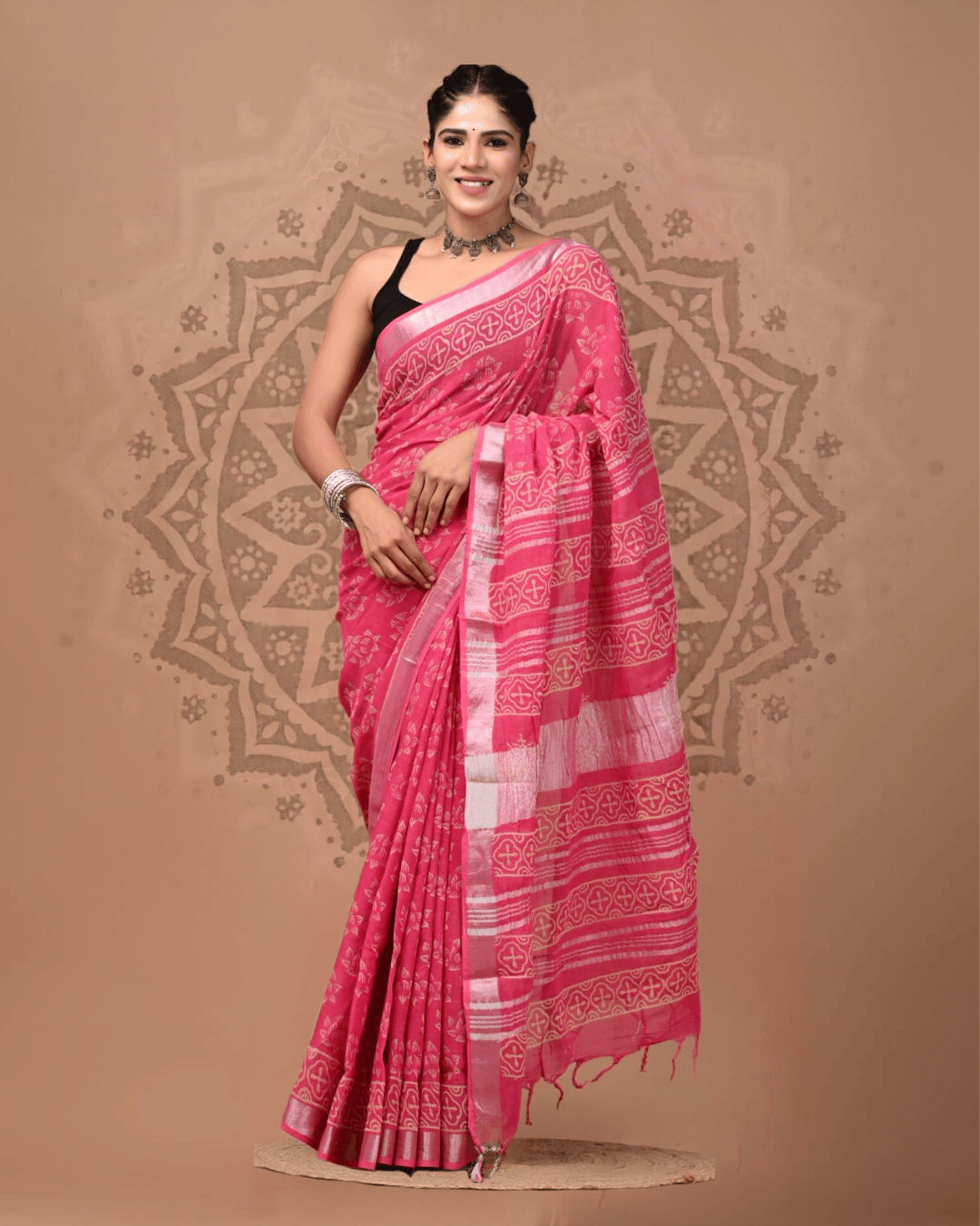 Rani-pink linen saree with muted gold-toned floral and quatrefoil-like motifs, a pale metallic-looking border, striped patterned pallu, and matching tassels.