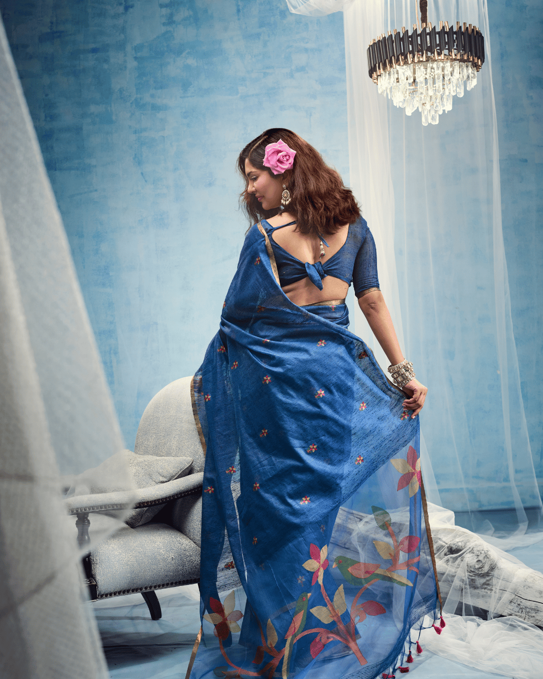 Back view shot of the royal blue ready to wear pocket saree adorned with large pink, coral, and green leaf-vine motifs and pink fringe tassels.