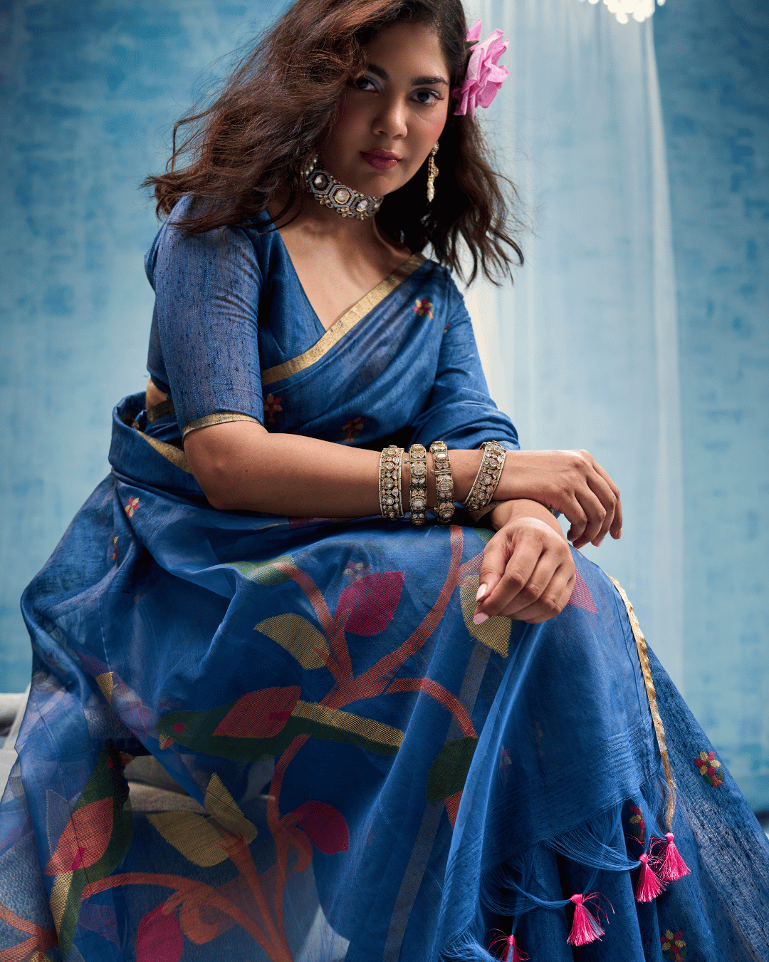 Seated shot of the leaf notes pre-stitched pocket saree, highlighting the soft munga-cotton texture and the vibrant floral-vine artwork spreading across the blue pallu.