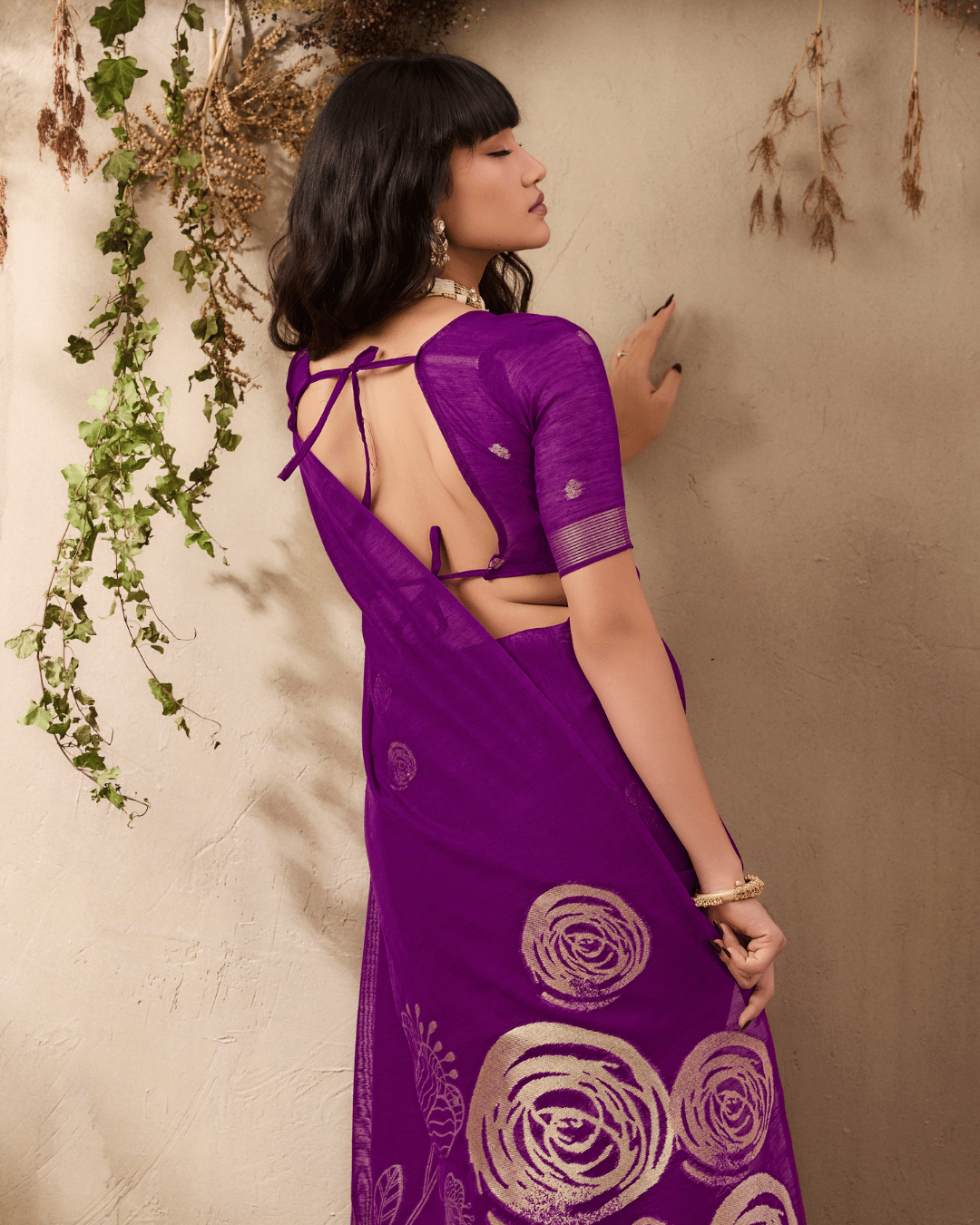 Model looking over her shoulder against a neutral wall, demonstrating the smooth fit across the waist and the large gold rose-and-leaf sketch artwork along the lower drape.